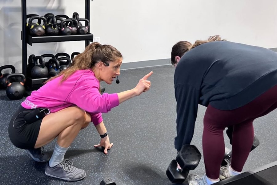 Caitlin crouched at floor level, correcting a client's deadlift form